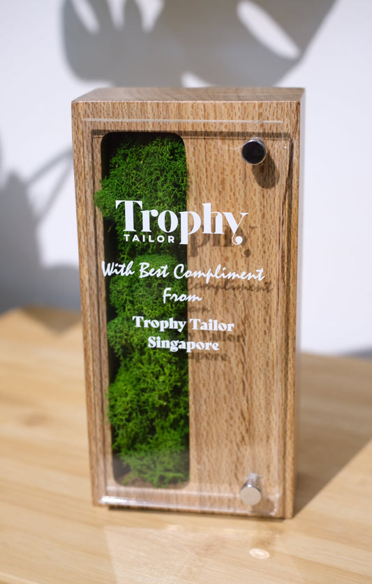 Wooden trophy with green moss-like material and 'Trophy Tailor' branding on a light wood background.