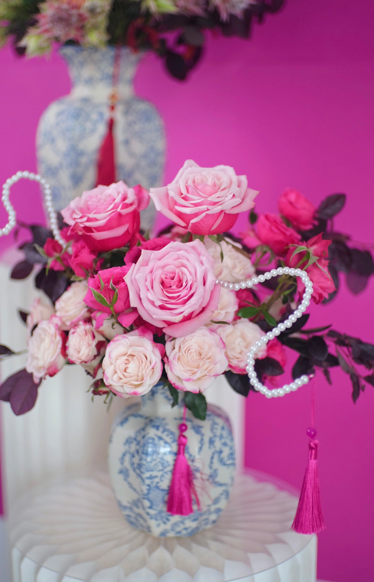 CNY floral arrangement features delicate pink roses and spray roses with deep burgundy accents and snake-like pearls in china porcelain vase close up 