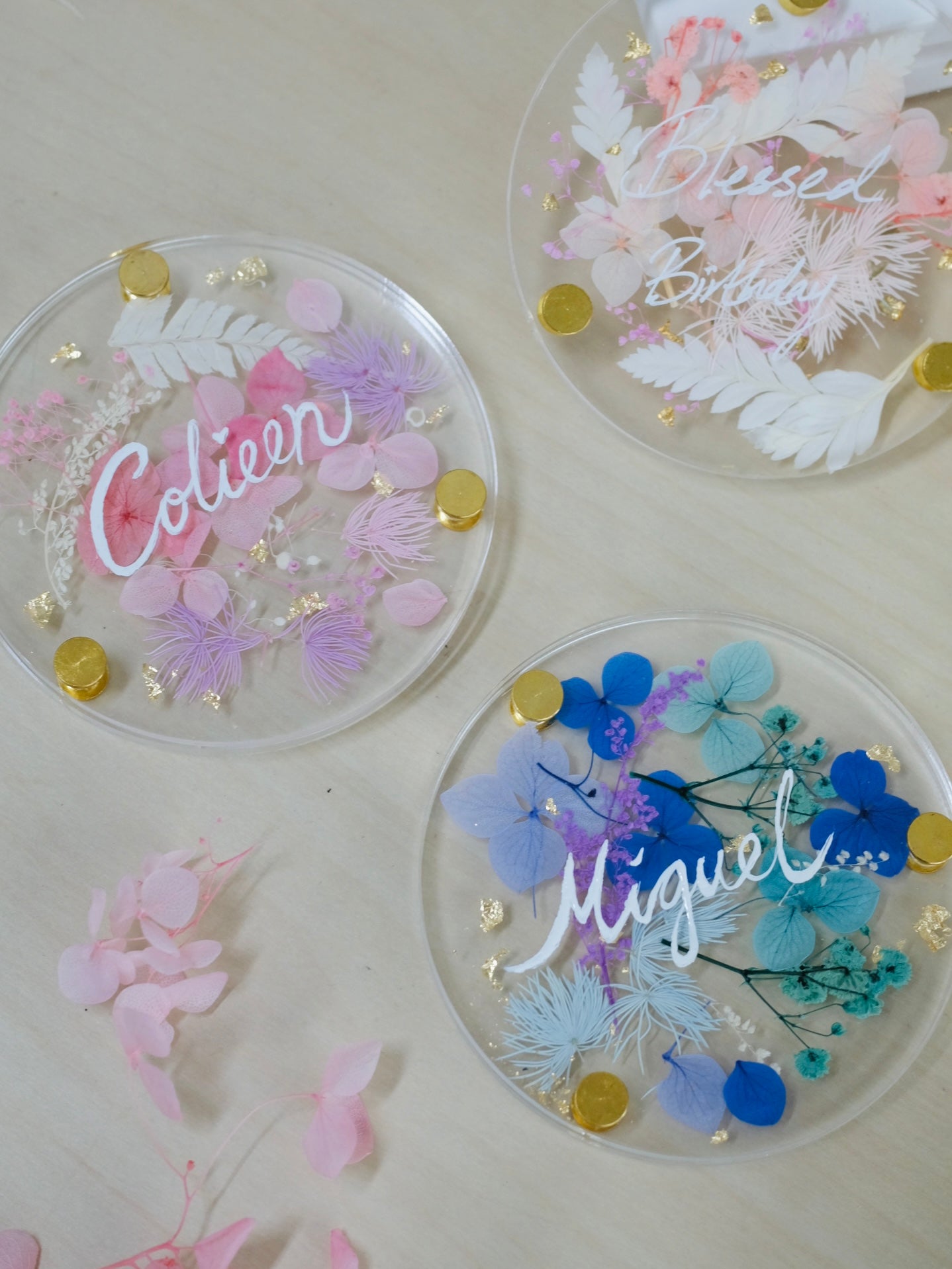 Three decorative coasters with floral designs and names 'Colleen', 'Miguel', and 'Bella' on a light background.