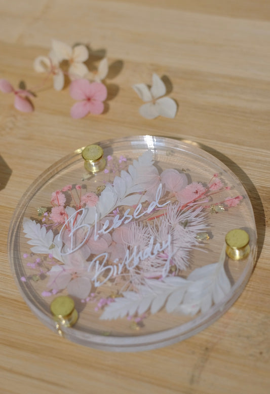 Decorative coaster with floral design and 'Blessed Birthday' text on a wooden surface.