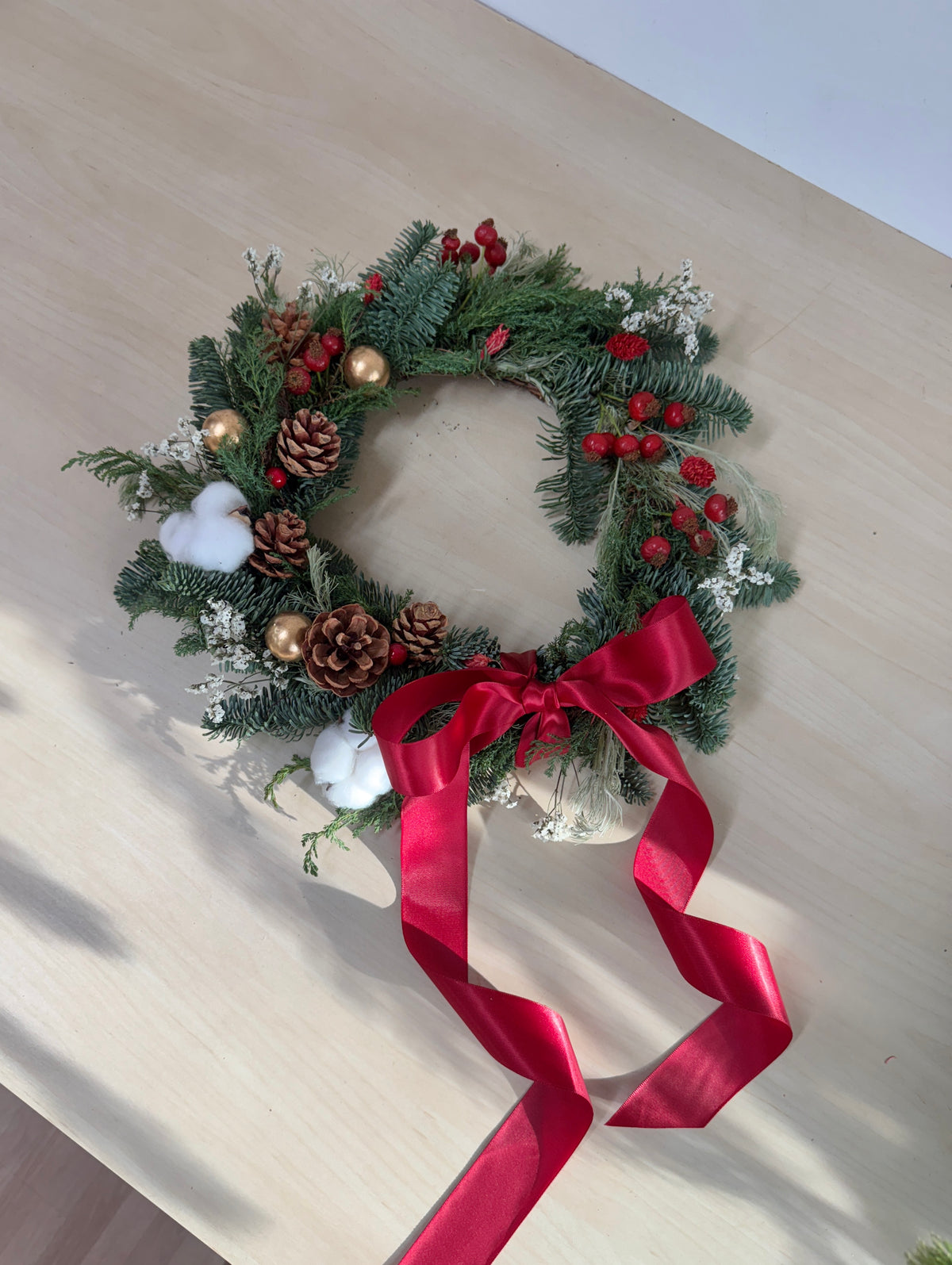 Finished fresh Christmas wreath with pine, cotton stems, berries and a trailing red ribbon