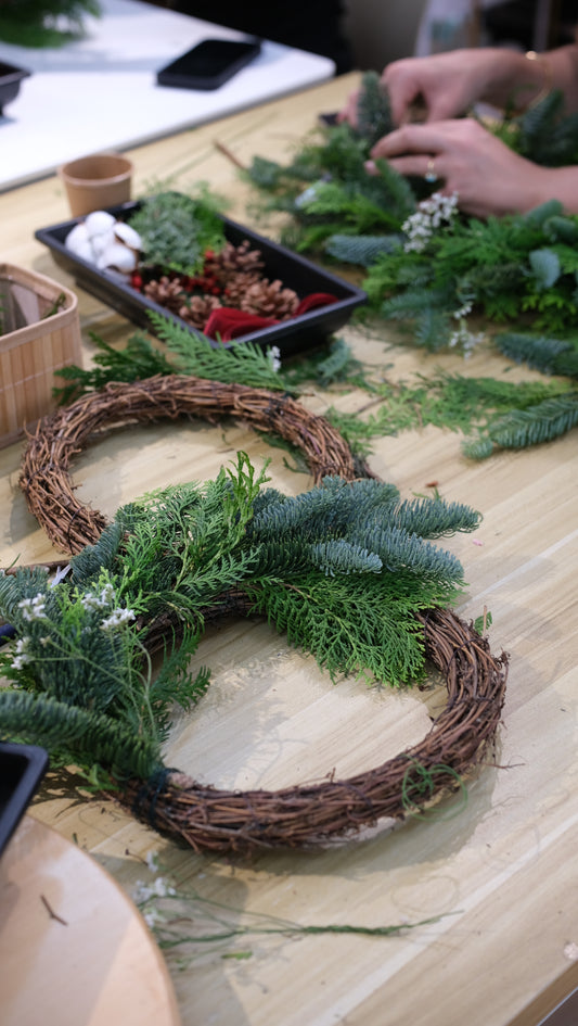 Fresh pine wreaths in progress on the studio table with trays of berries and pinecones