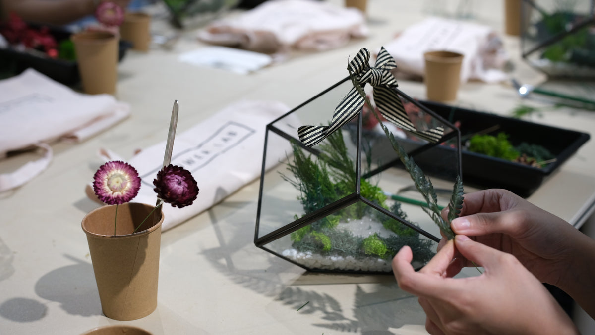 Hands assembling a preserved flower terrarium on the workshop table